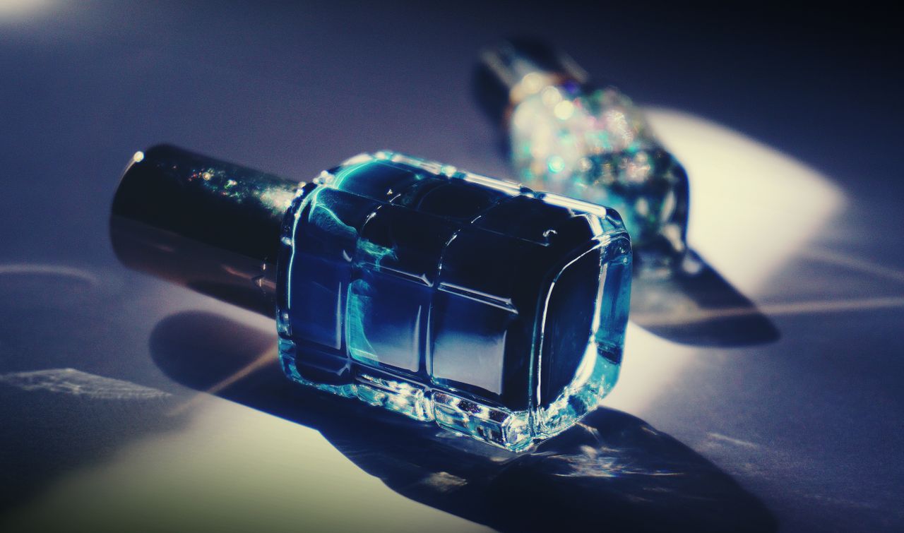 Close-up of a luxurious blue nail polish bottle casting a reflection.