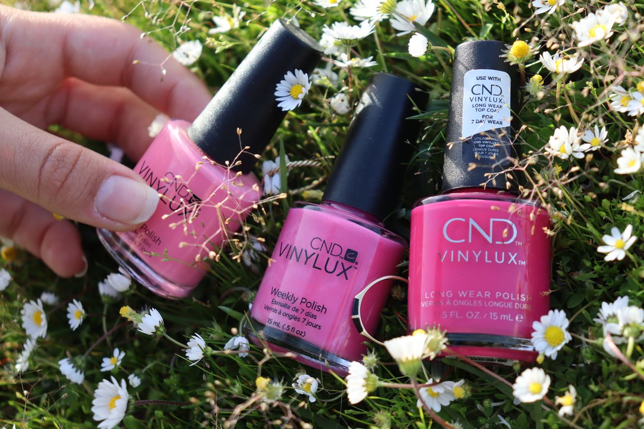 Vibrant pink nail polish bottles in a fresh outdoor setting with daisies, showcasing beauty and nature.