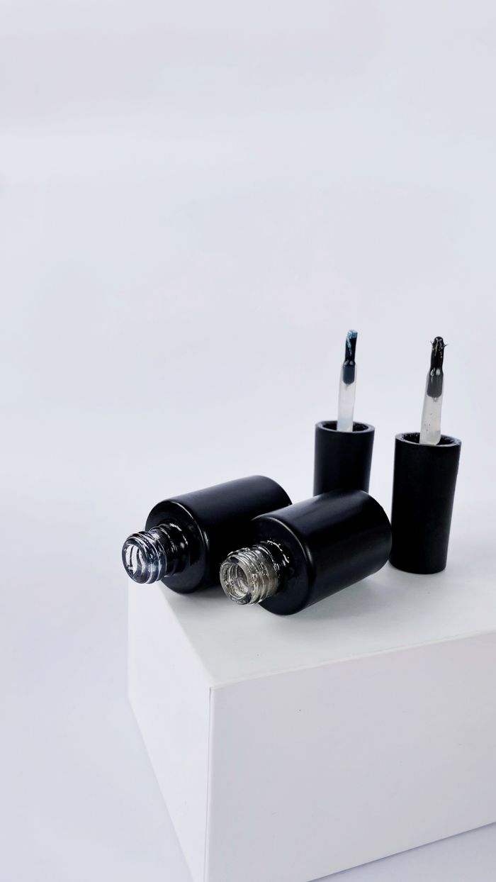 Minimalist display of black nail polish bottles with applicators on a white background, ideal for beauty and design themes.