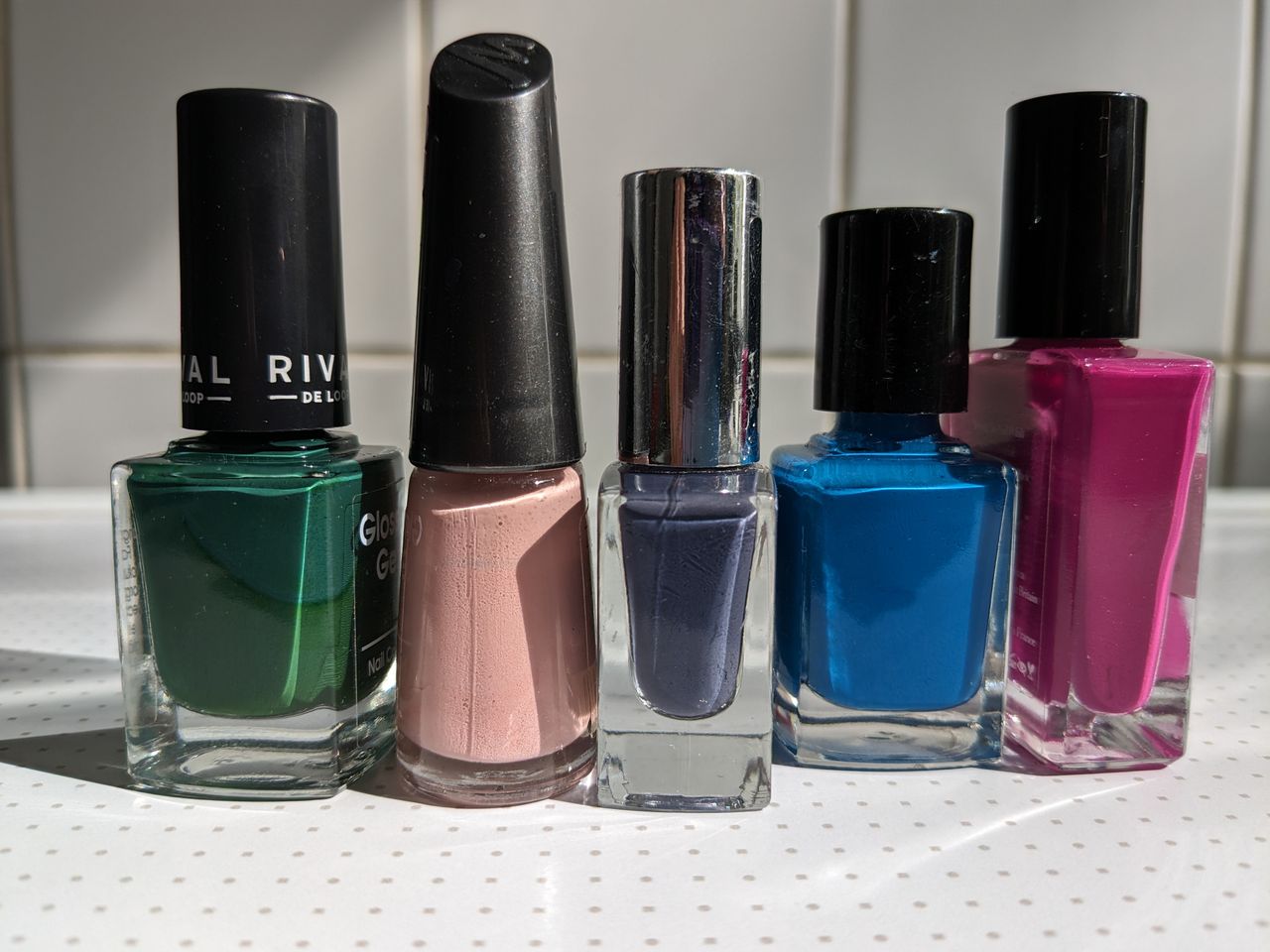 services-02 Five vibrant nail polish bottles arranged neatly on a light background.